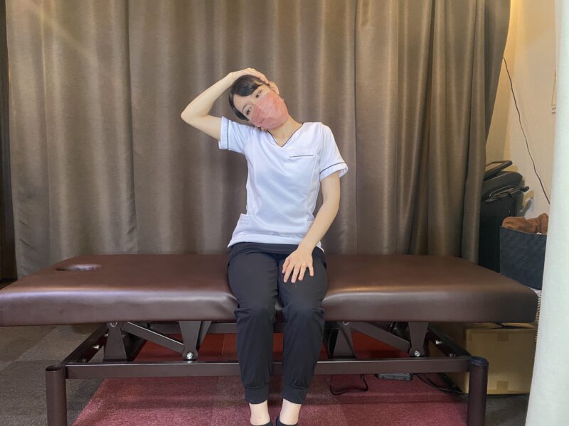 座って頭を横へ傾け、片手を頭に添えた首のストレッチ