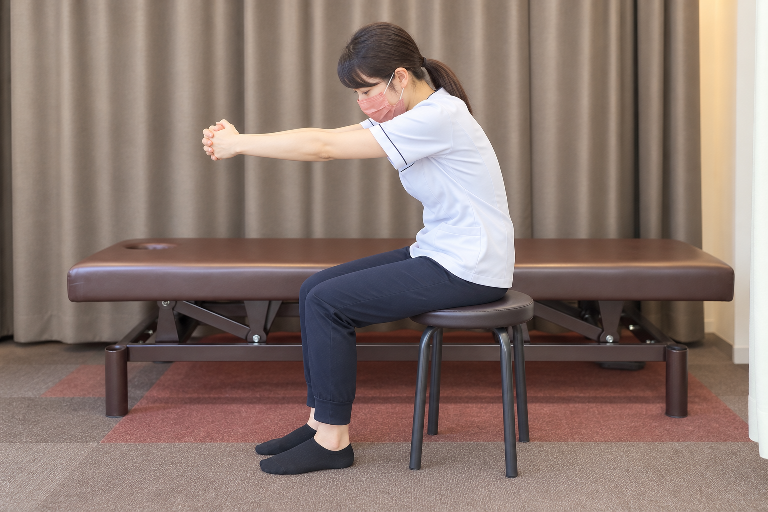椅子に座り組んだ両手を前へ伸ばし背中を丸める姿勢(AI生成イメージ)